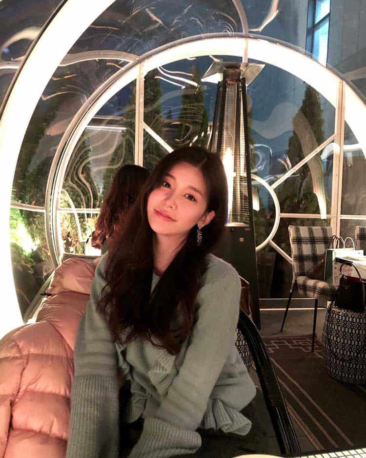 Young woman at EJH Distribution event, illuminated modern decor, stylish casual outfit, happy expression, vibrant setting, focus on joyful atmosphere.