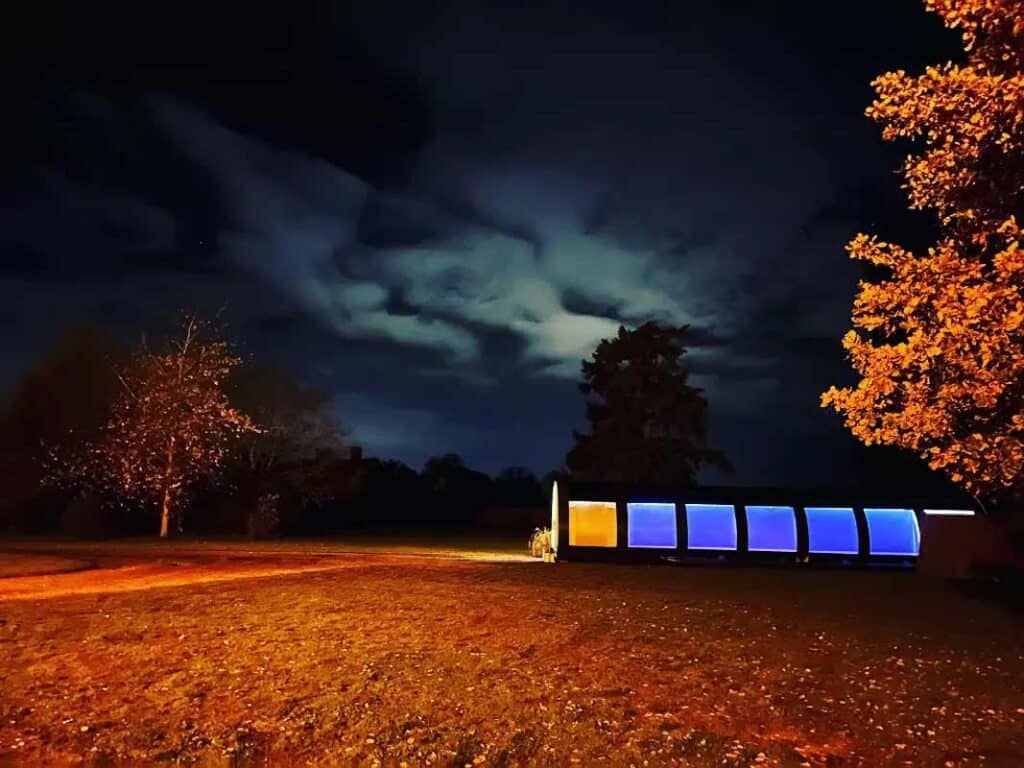 Night outdoor scene with illuminated containers and trees with autumn foliage.