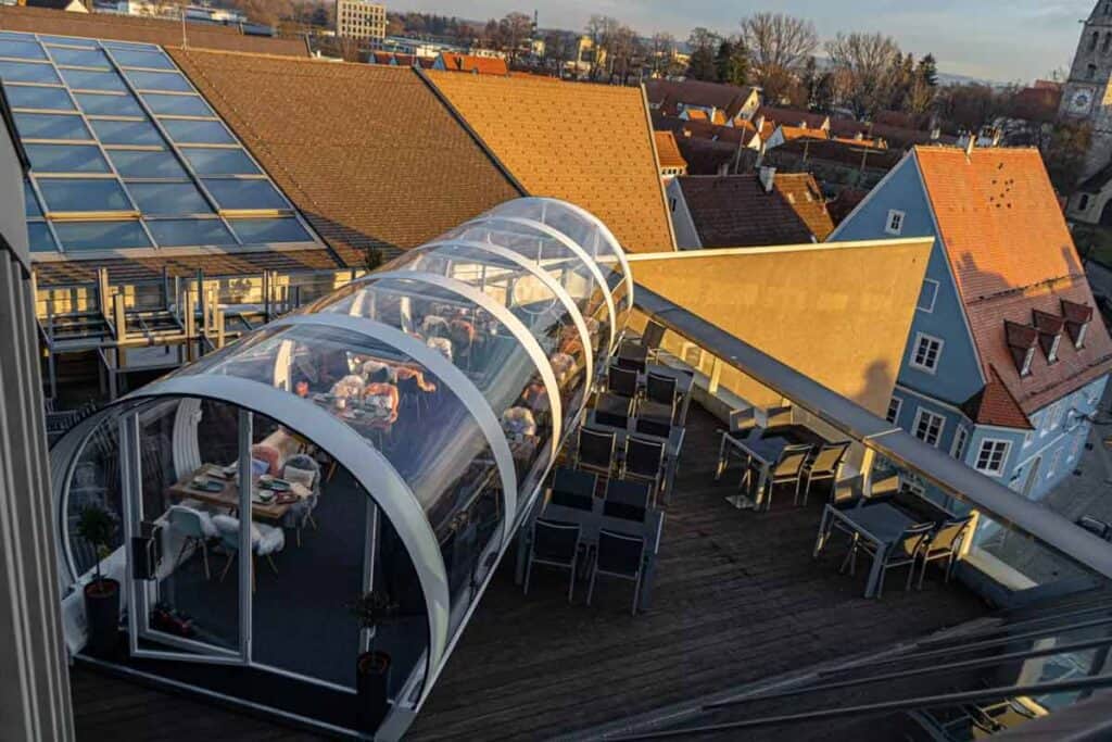 Aerial view of rooftop restaurant with glass-enclosed dining area and outdoor seating, overlooking a historic town.