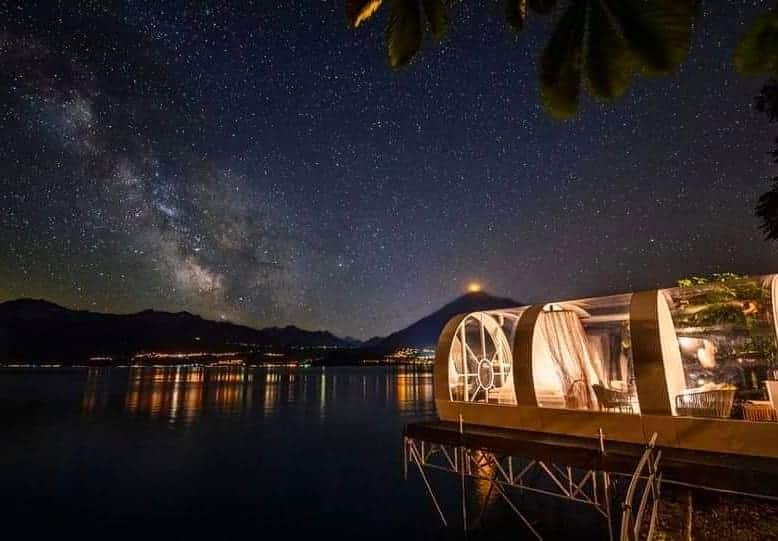 Stargazing at night over lake with mountain views and illuminated glass pavilion.