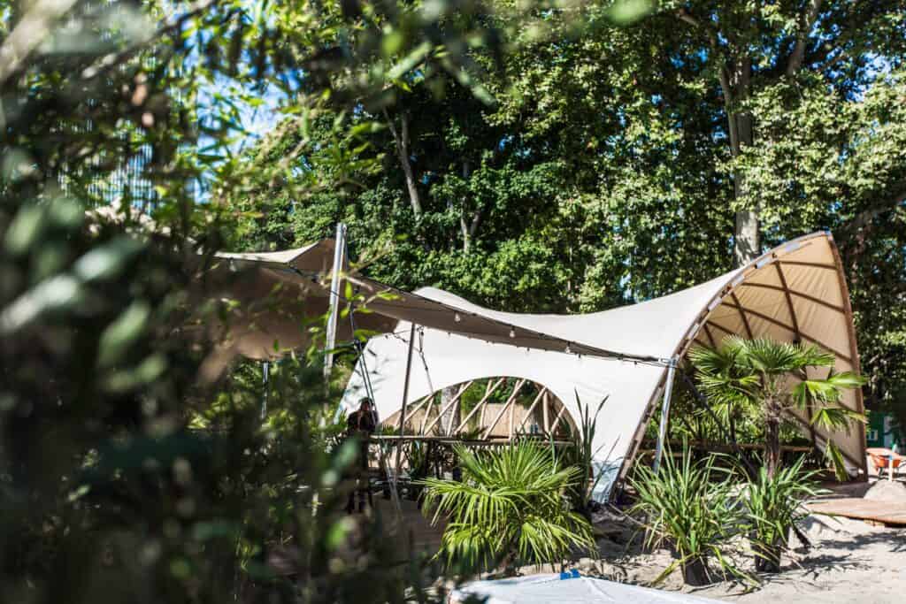 Eco-friendly outdoor event space with modern tensile fabric canopy and lush greenery.