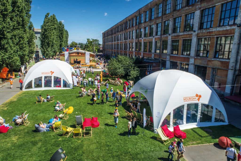 An outdoor experiential marketing event featuring branded tents, interactive activities, and attendees engaging in brand experiences on a sunny day.