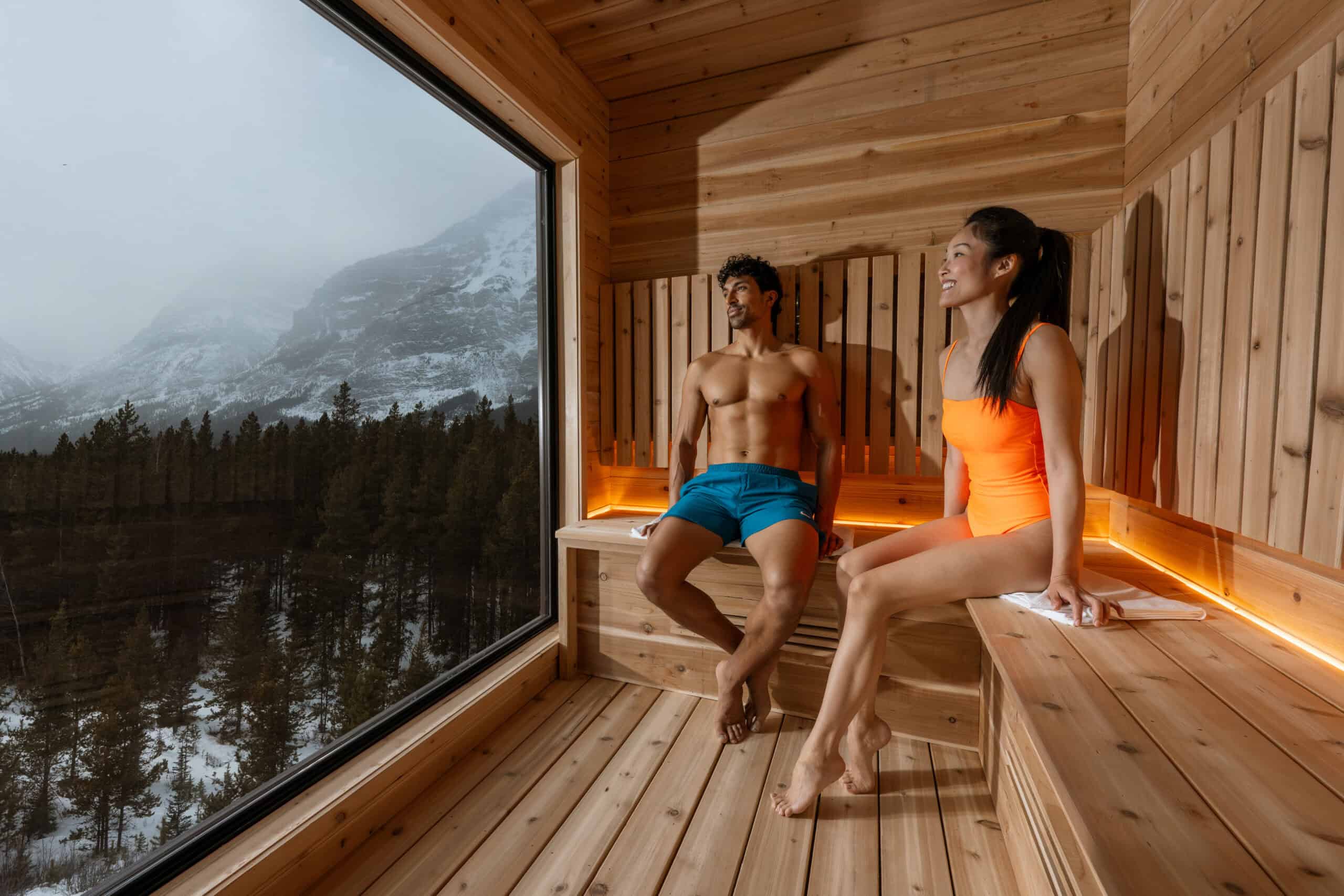 Relaxing sauna with two people enjoying the scenic mountain landscape through a large window.