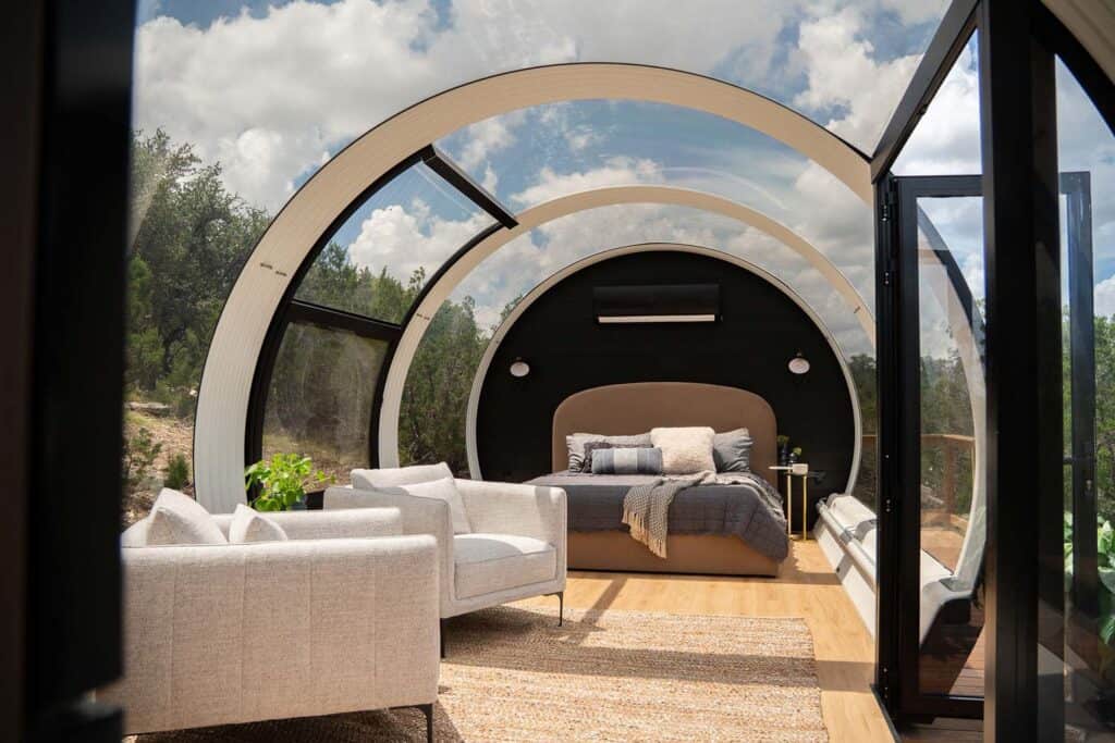 Bright, stylish bedroom with glass walls, circular architecture, and comfortable bed in a scenic outdoor setting.